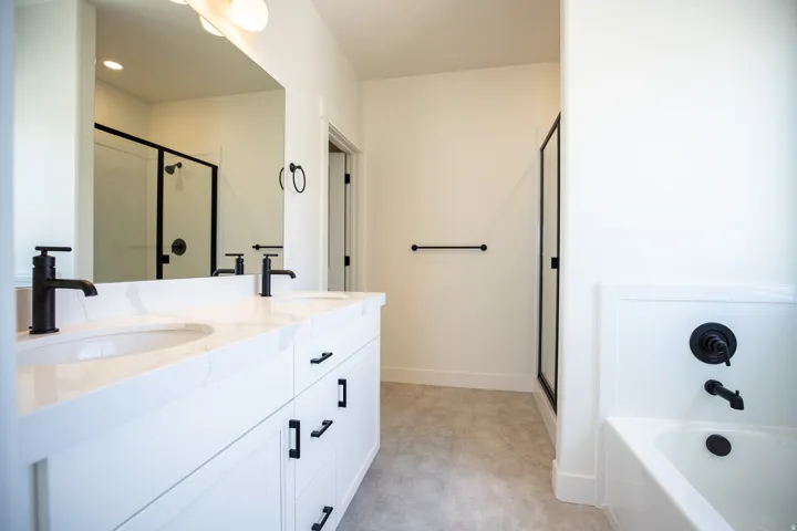 Primary bath with dual sinks, painted white wood cabinets, quartz slab countertop, soaker tub and large walk-in shower.