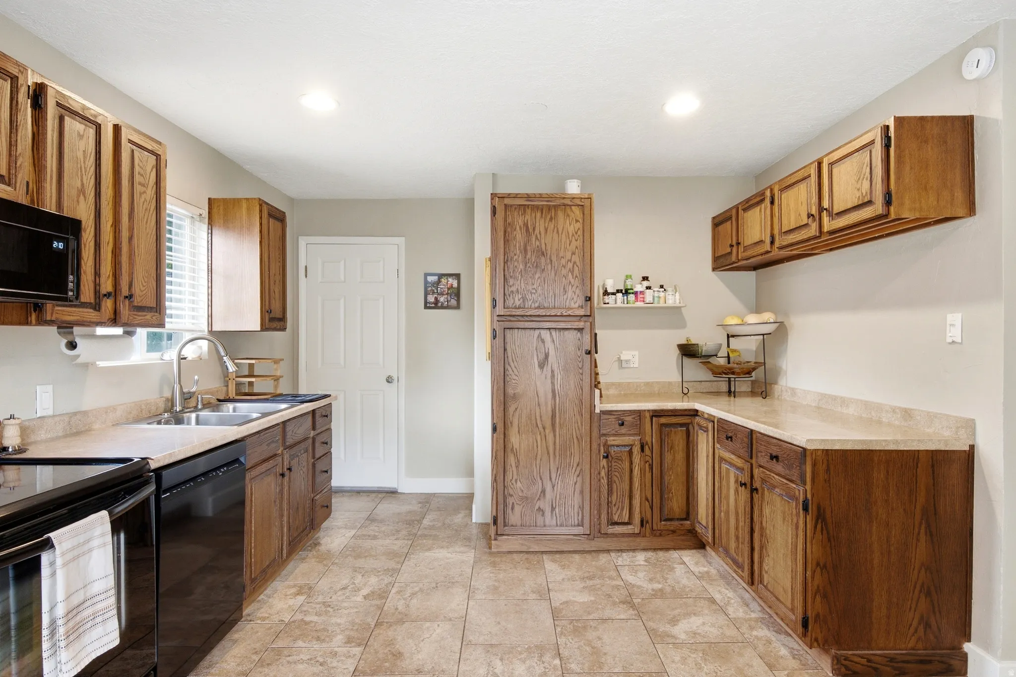 Kitchen featuring wood cabinetry, stone-finish countertops, stainless steel sink with gooseneck faucet, black appliances, and tile flooring