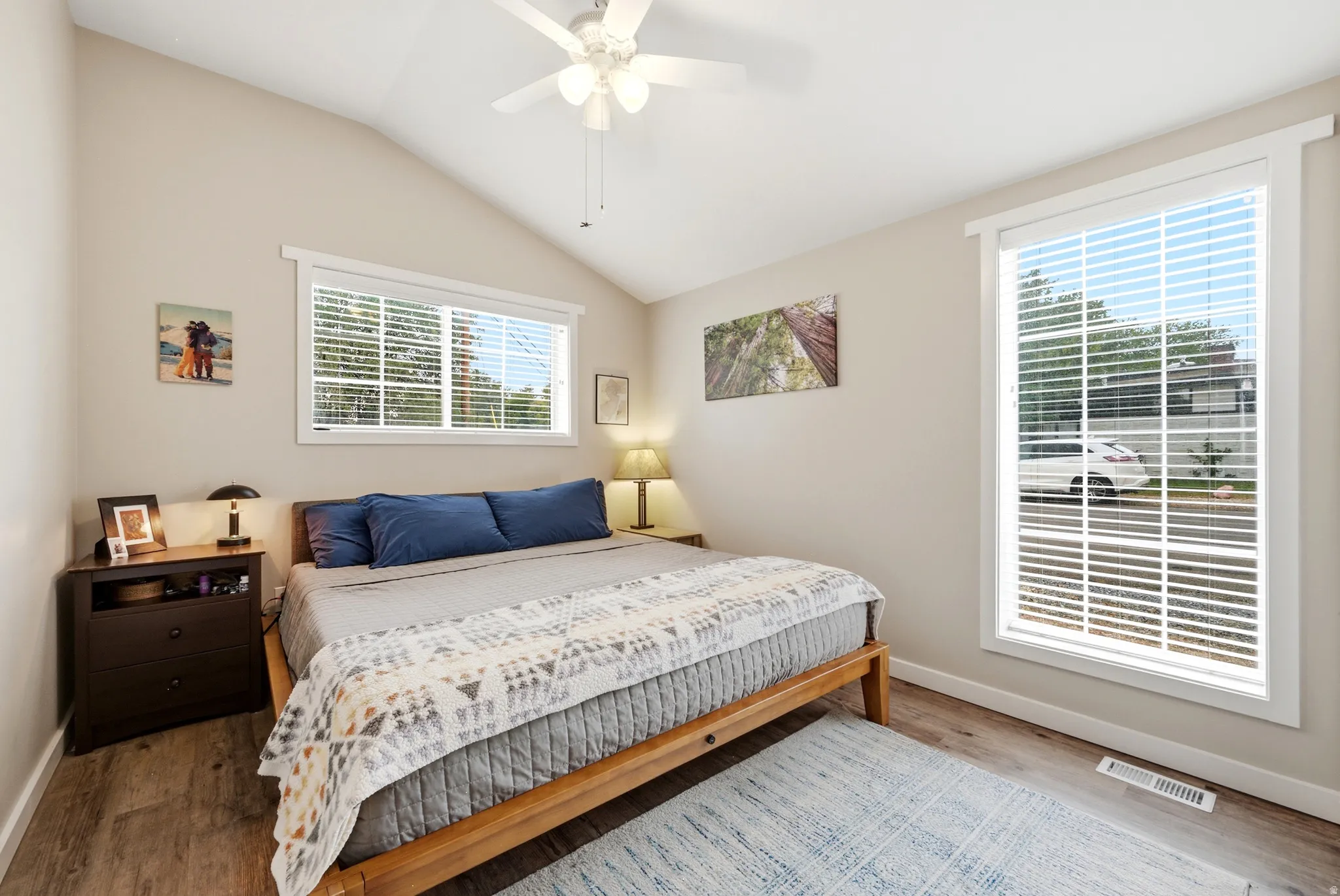 Vaulted ceilings, wood-finish flooring, white trim windows, and a ceiling fan