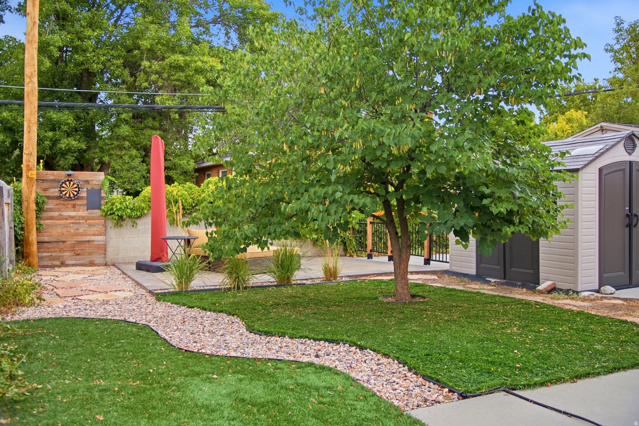 Manicured lawn, stone pathway, built-in storage shed, concrete patio area, and mature tree