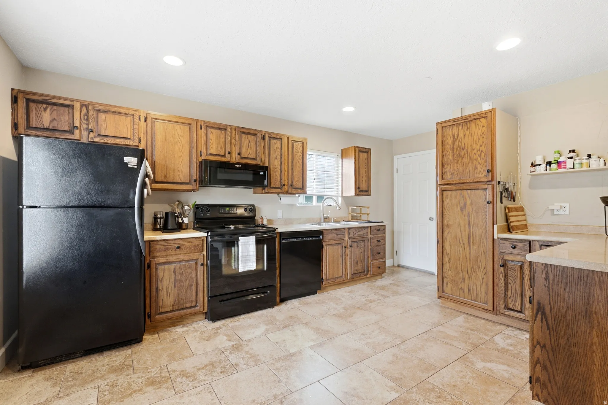 Kitchen featuring wood-finish cabinetry, black appliances, a double basin sink, and recessed lighting