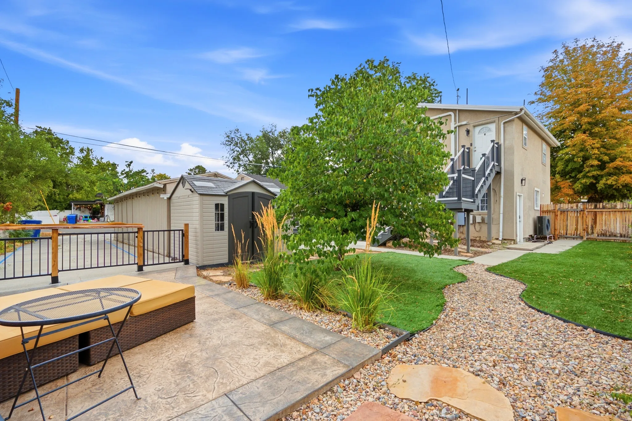 Expansive backyard featuring a stamped concrete patio, manicured lawn, gravel pathway, and two storage sheds