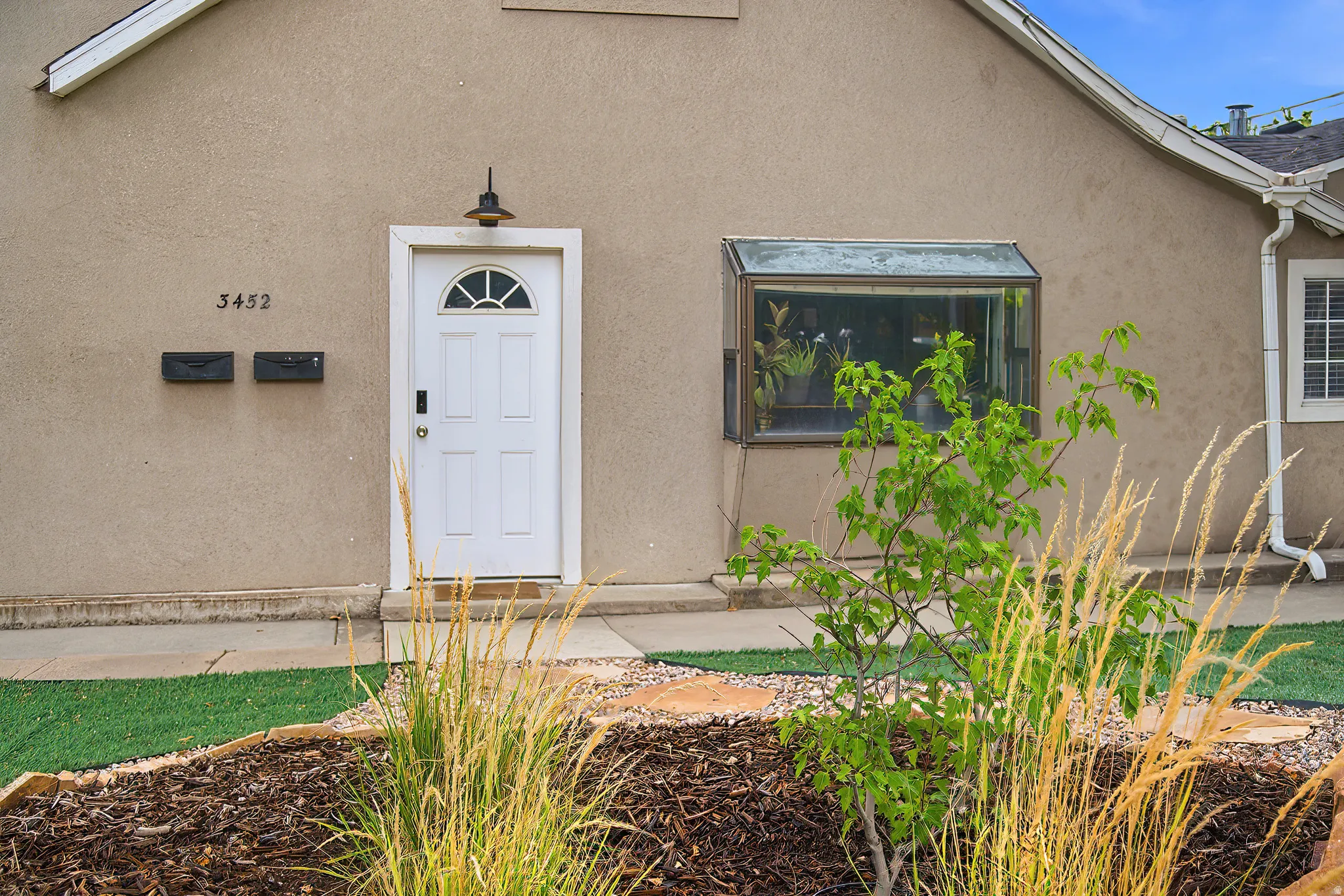 Stucco exterior featuring a white paneled entry door with an arched transom, a box window, and a gutter system