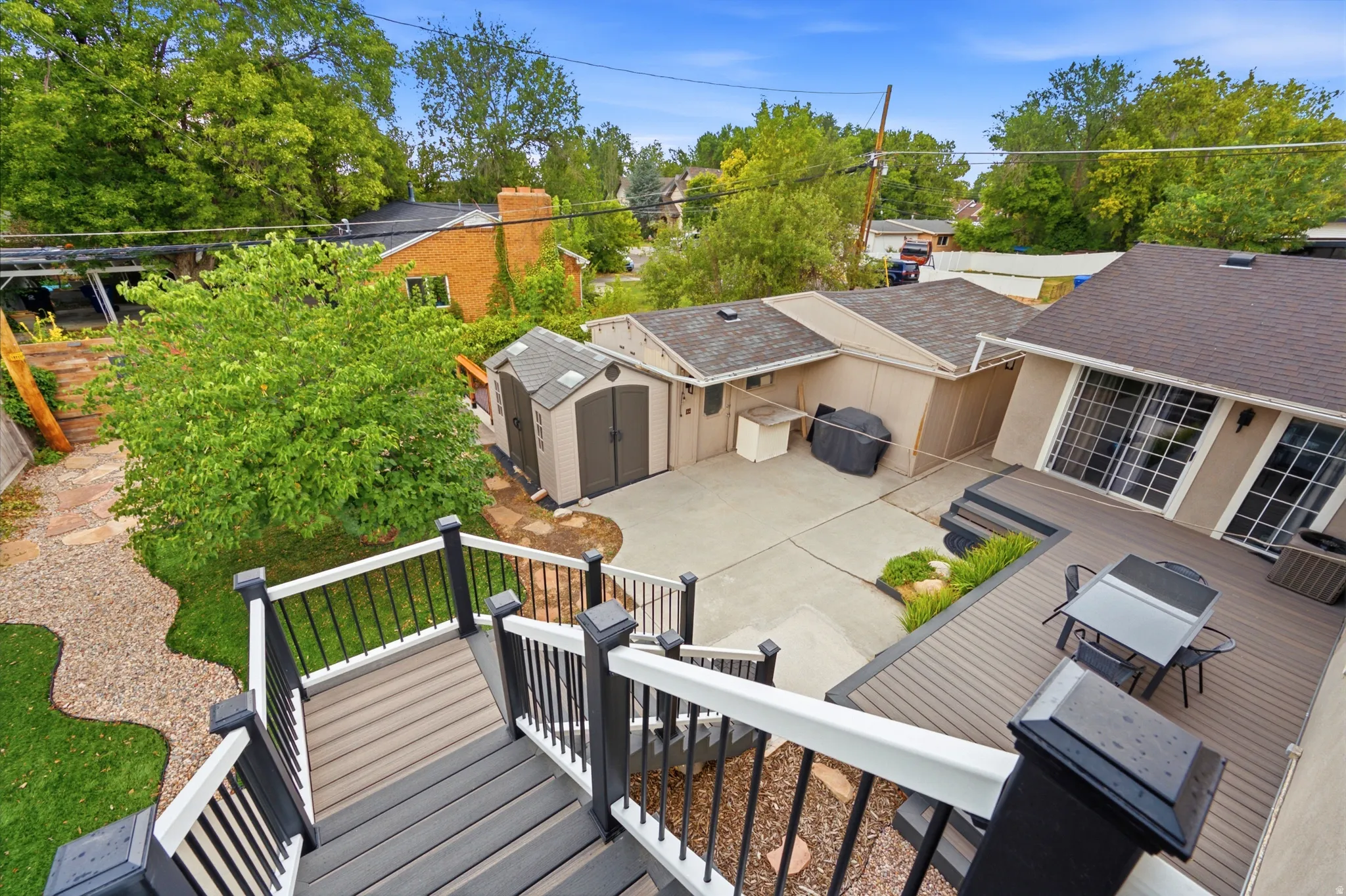 Multi-level outdoor decking, composite decking materials, concrete patio area, two storage sheds, and mature landscaping