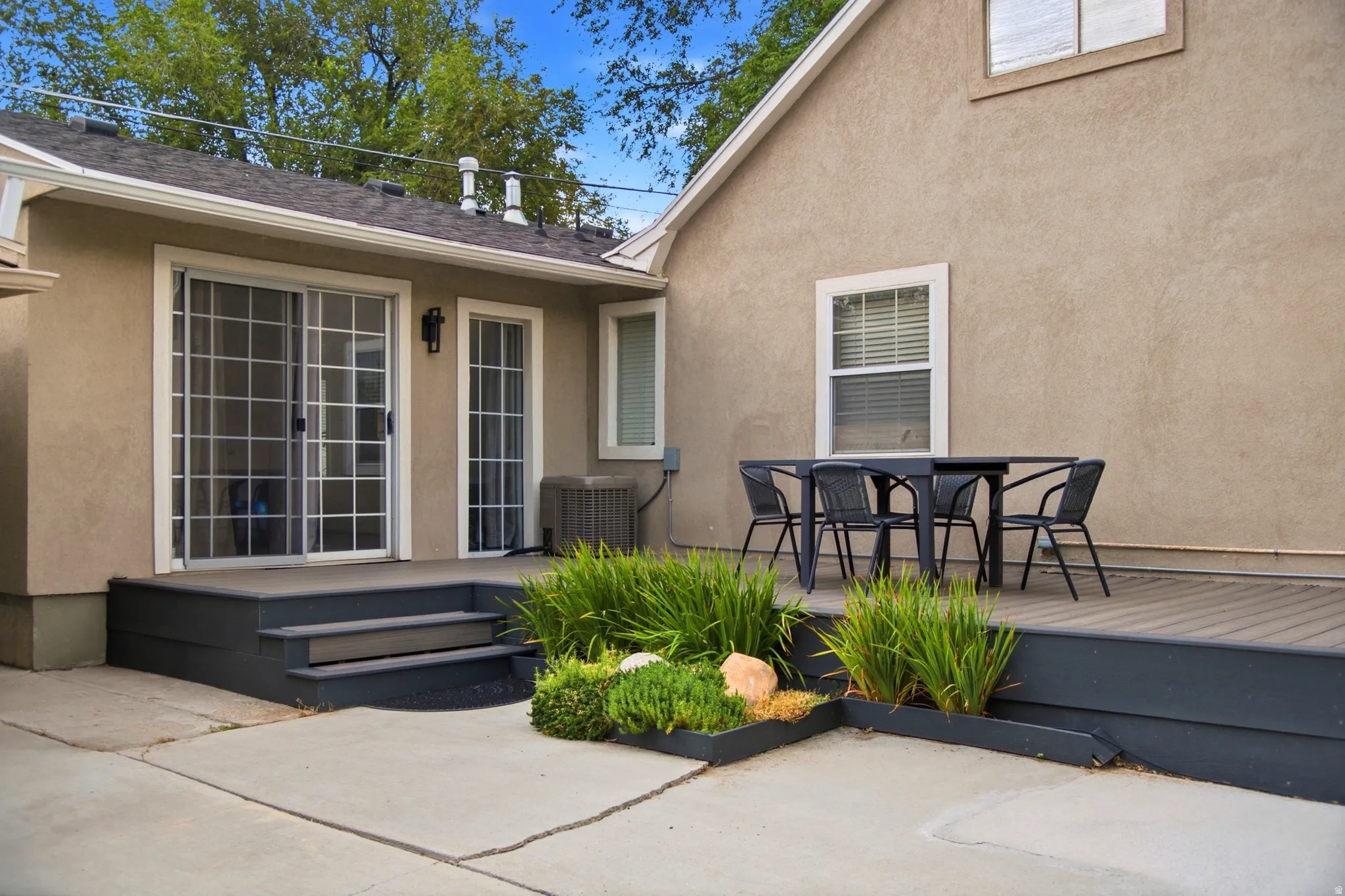 Stucco exterior with a multi-level deck, concrete patio, sliding glass door, and integrated planter beds