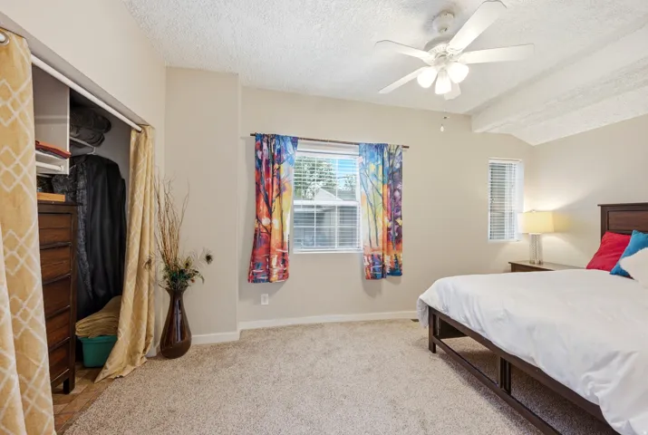 Carpeted flooring, vaulted ceiling with exposed beams, ceiling fan with light fixture, window with blinds
