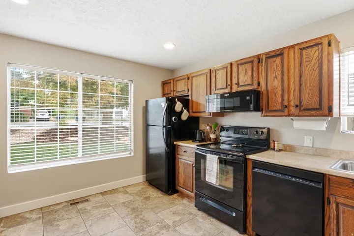 Kitchen featuring wood cabinetry, black appliances, a double basin sink, and tile flooring
