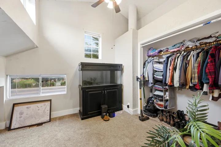 Vaulted ceiling with a ceiling fan, multiple windows, and a built-in closet with shelving