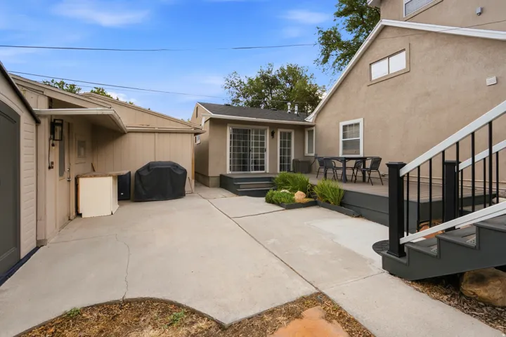 Expansive concrete patio with a raised deck, featuring sliding glass doors and exterior lighting