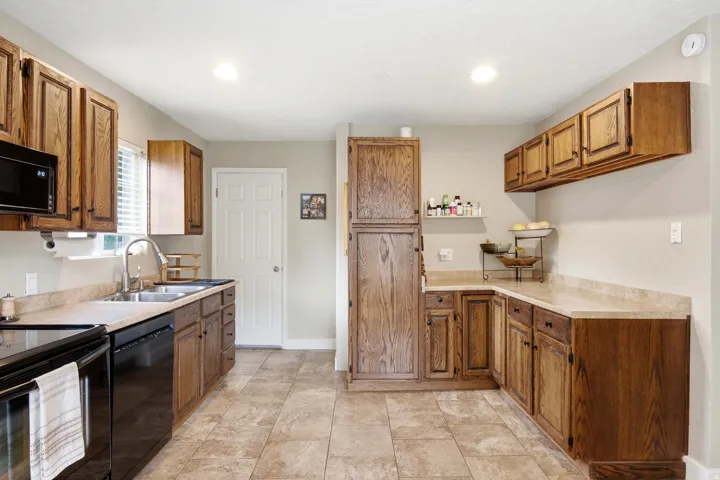 Kitchen featuring wood cabinetry, stone-finish countertops, stainless steel sink with gooseneck faucet, black appliances, and tile flooring
