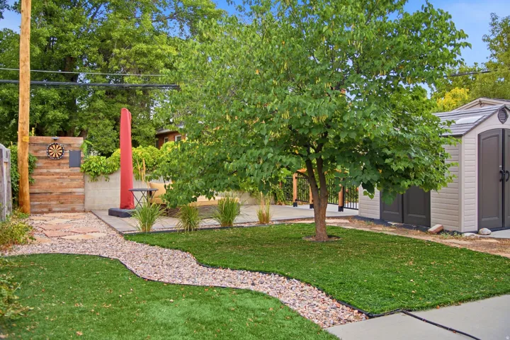 Manicured lawn, stone pathway, built-in storage shed, concrete patio area, and mature tree