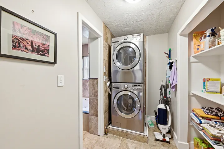 Compact laundry area featuring stacked front-load machines, tiled flooring, and built-in shelving