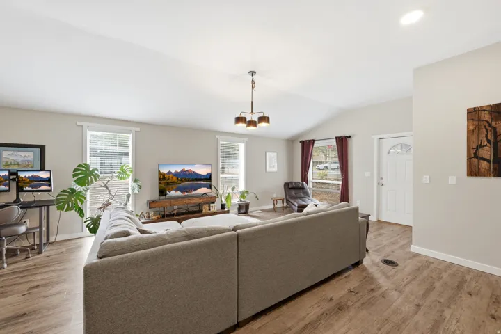 Vaulted ceiling with a contemporary light fixture, wood-finish flooring, multiple windows, and a white paneled entry door