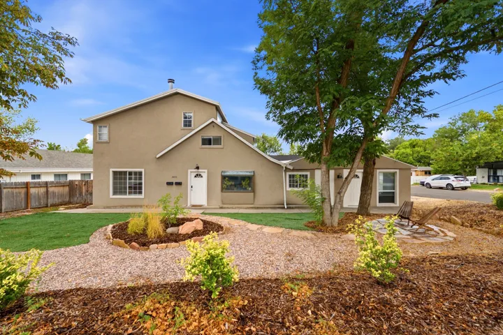 Stucco exterior with multiple window styles, established tree, and a circular landscaped bed