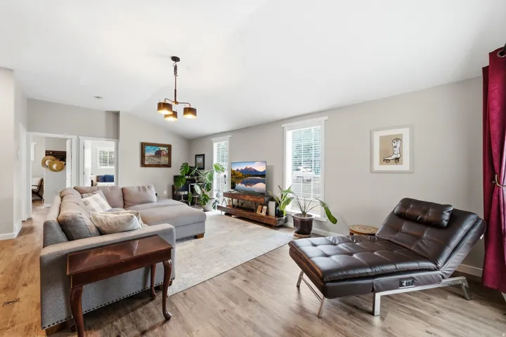 Vaulted ceiling with a pendant light fixture, wood-finish flooring, and multiple windows with blinds
