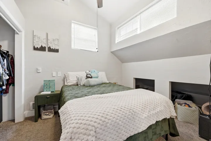 Sloped ceiling with an integrated ceiling fan, carpeted flooring, and a built-in closet