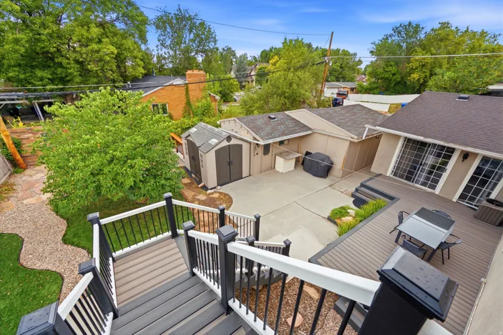 Multi-level outdoor decking, composite decking materials, concrete patio area, two storage sheds, and mature landscaping