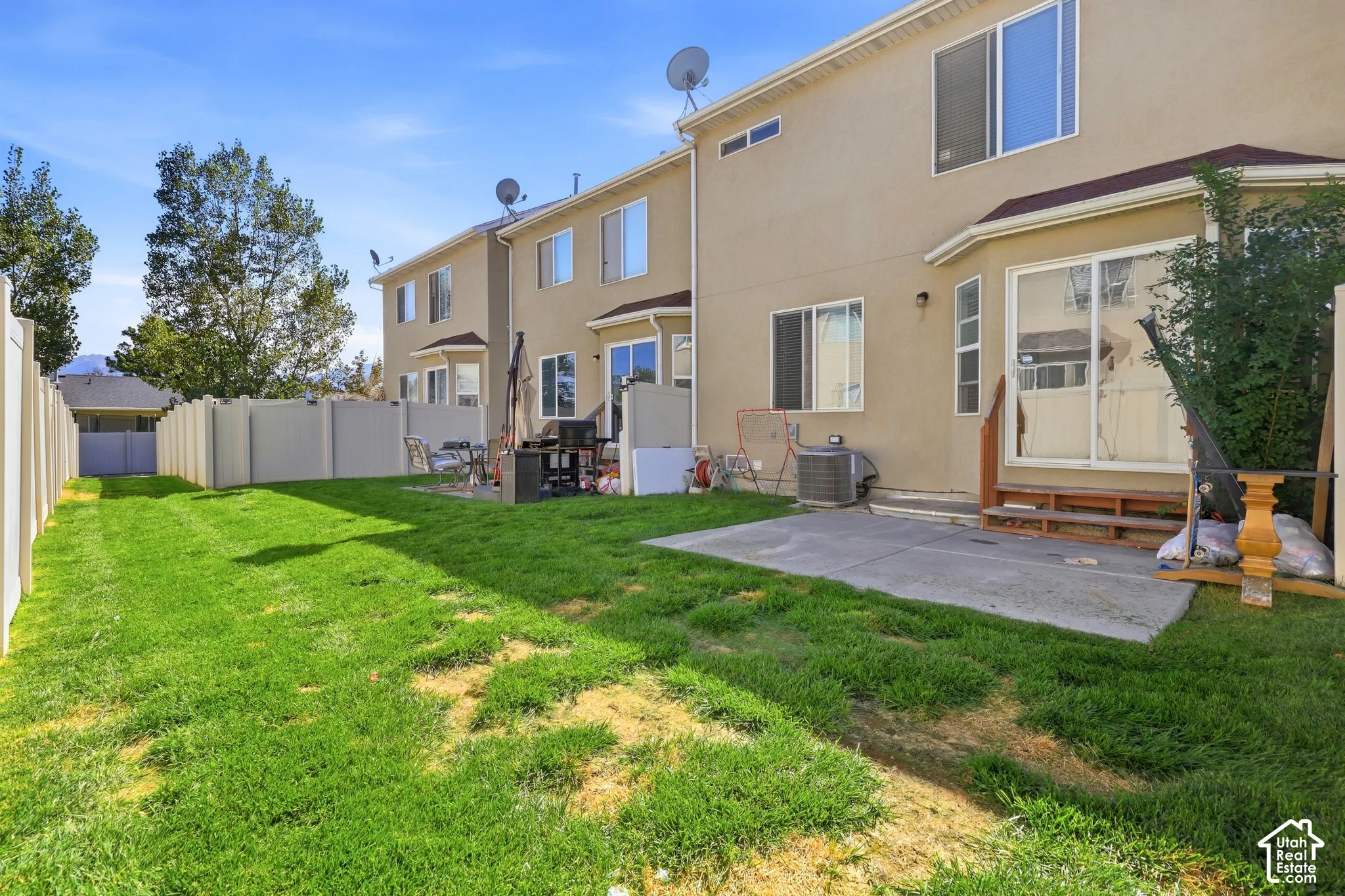 Expansive grass lawn with a concrete patio, vinyl fencing, and multiple windows