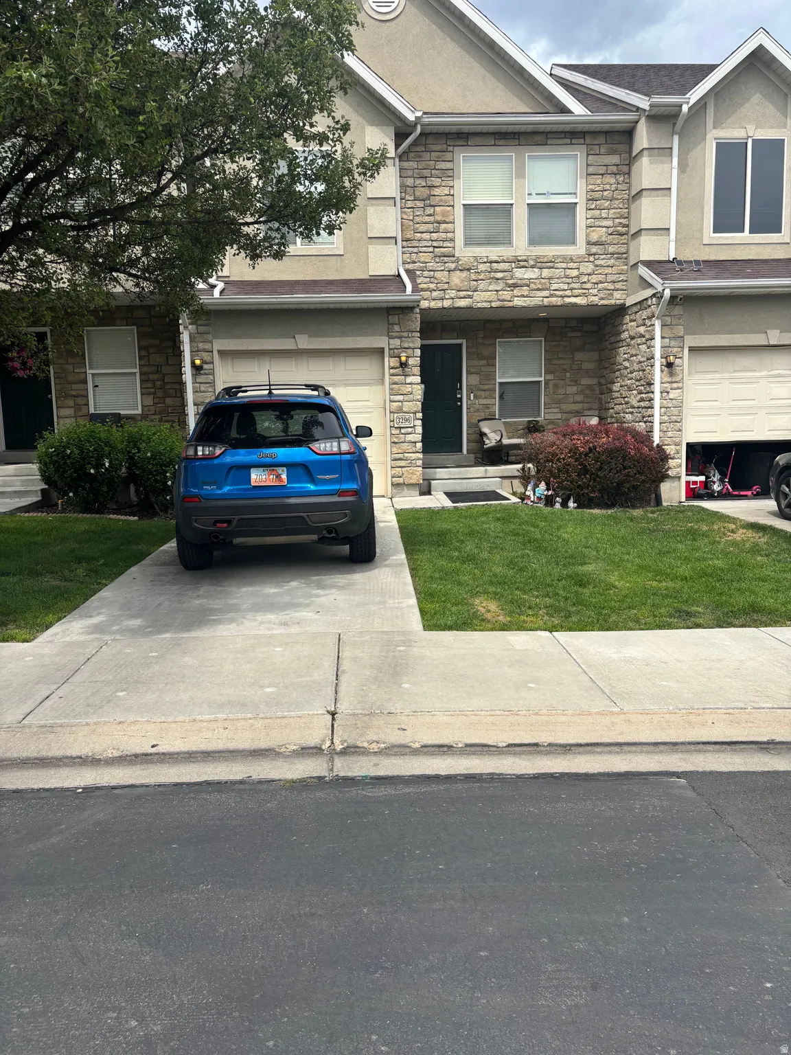 Stone facade with stucco accents, attached garage, concrete driveway, front entrance, and maintained lawn area