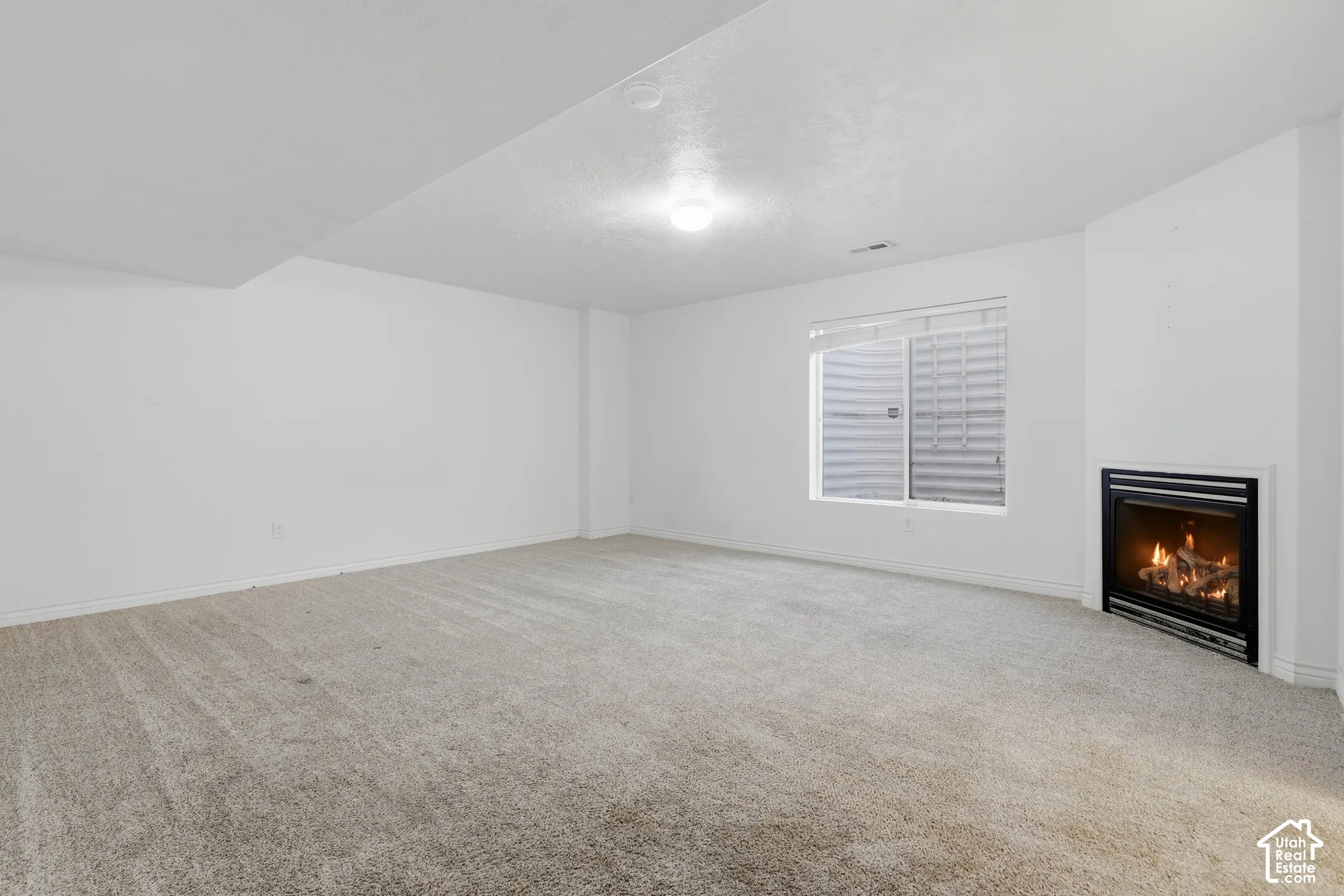 Recessed fireplace with black surround, soft carpet flooring, and a single window