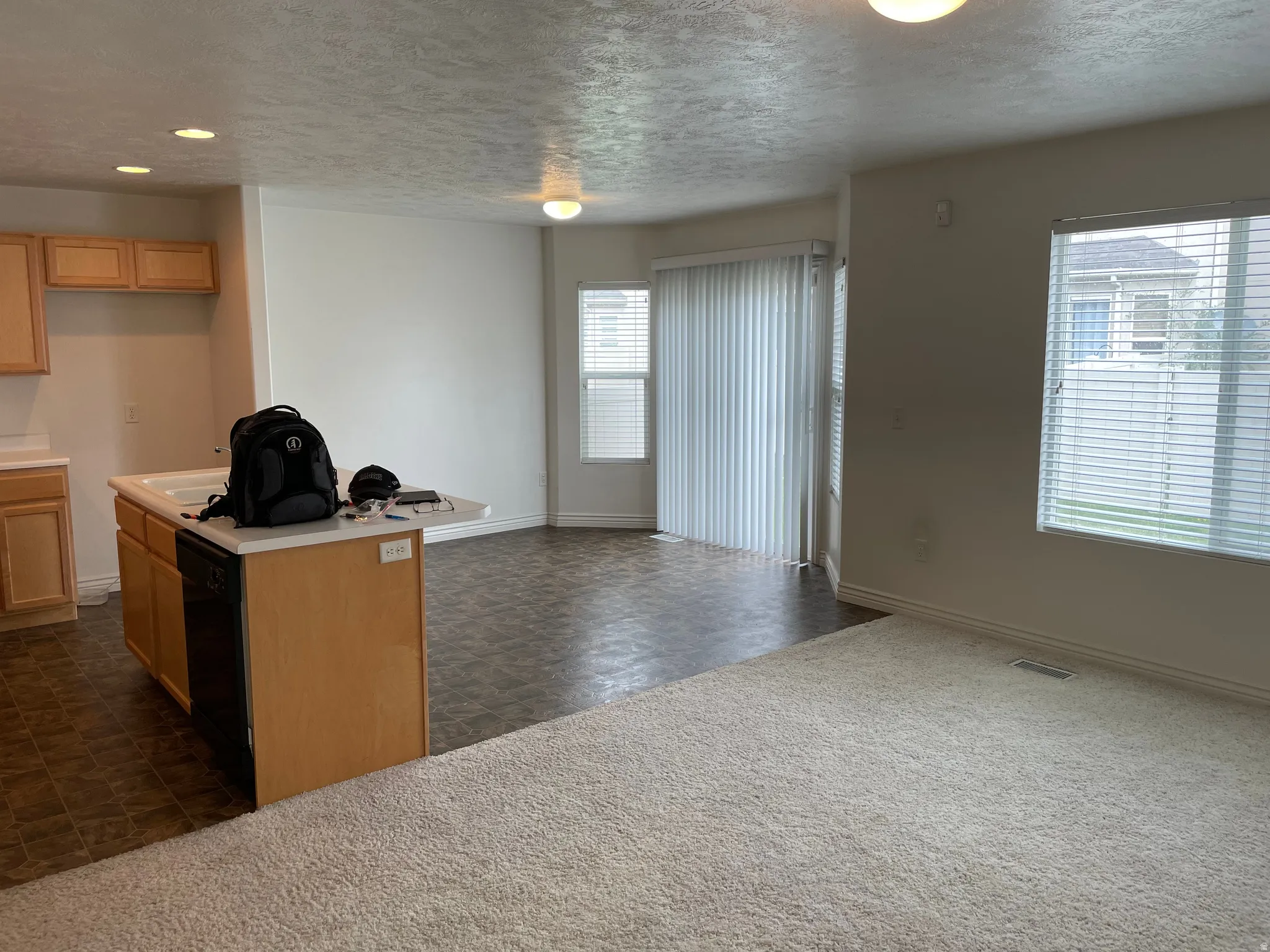 Open-concept layout featuring a kitchen island with integrated sink, recessed lighting, slider door, and window with blinds