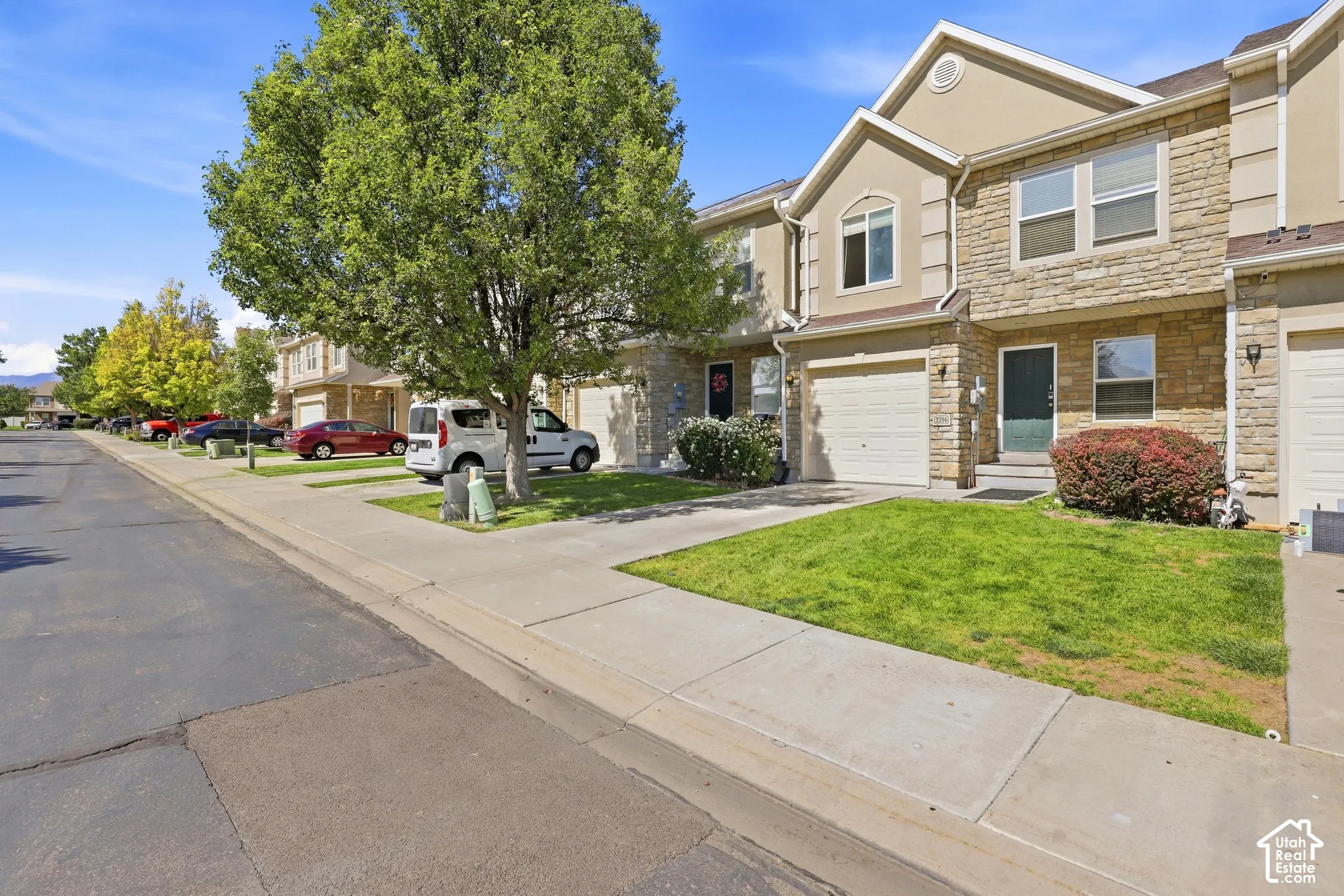 Stone and stucco exterior, attached garage, front entrance, established landscaping, and paved street