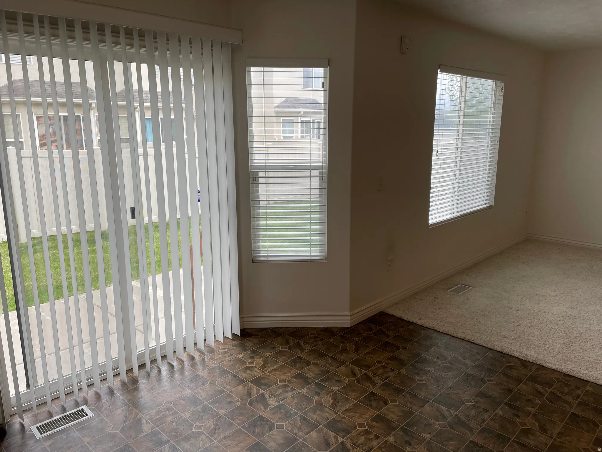 Sliding glass patio door, two windows with blinds, carpeted floor, and tiled floor