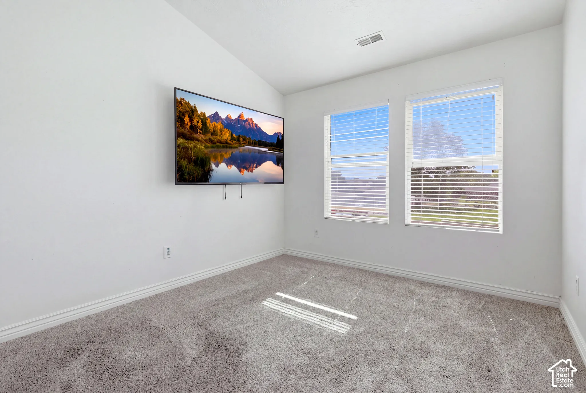 White walls, two windows with blinds, and light-toned carpeting