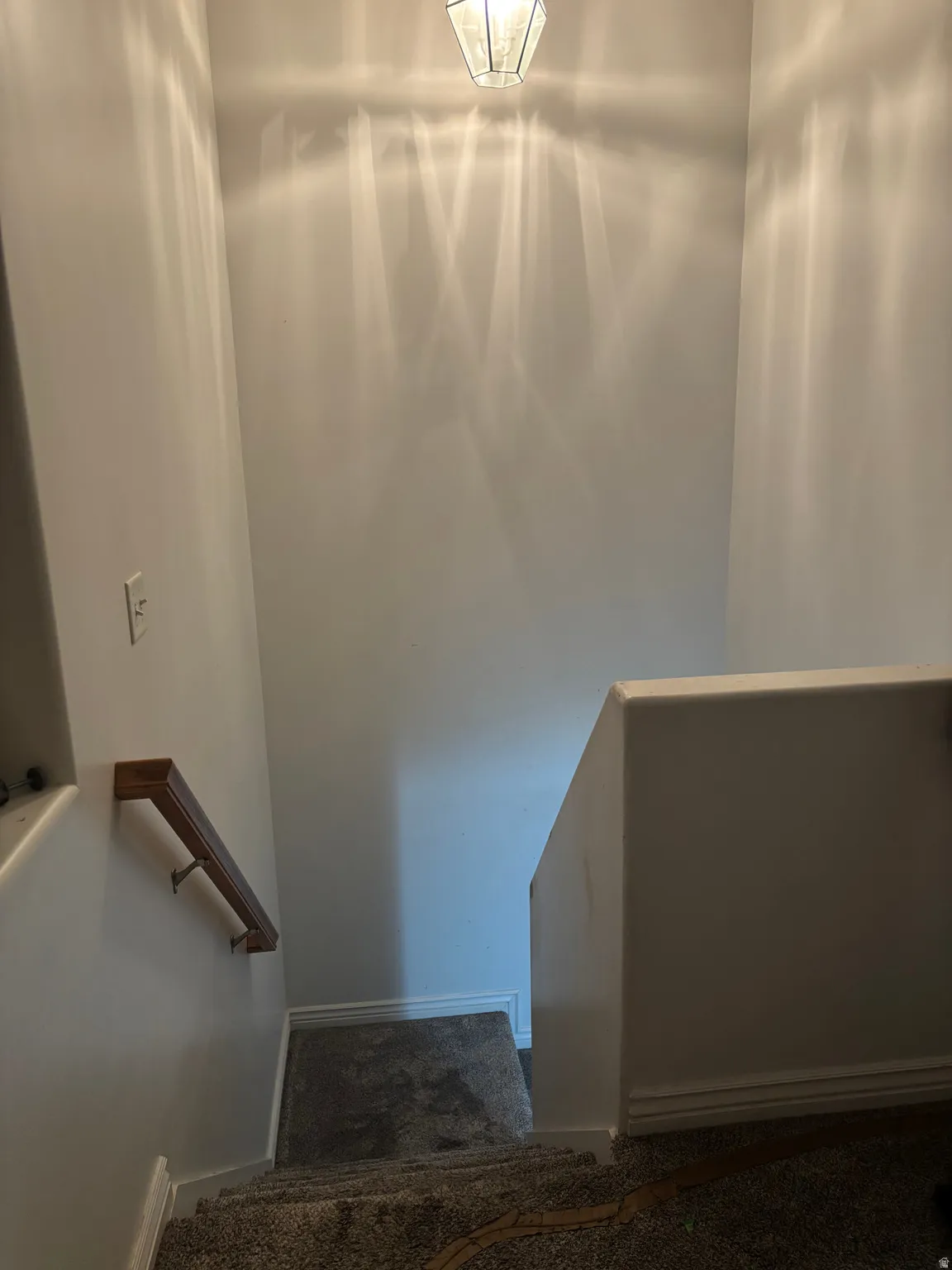 Stairwell with carpeted steps, a wood-finish handrail, white walls, and an overhead light fixture