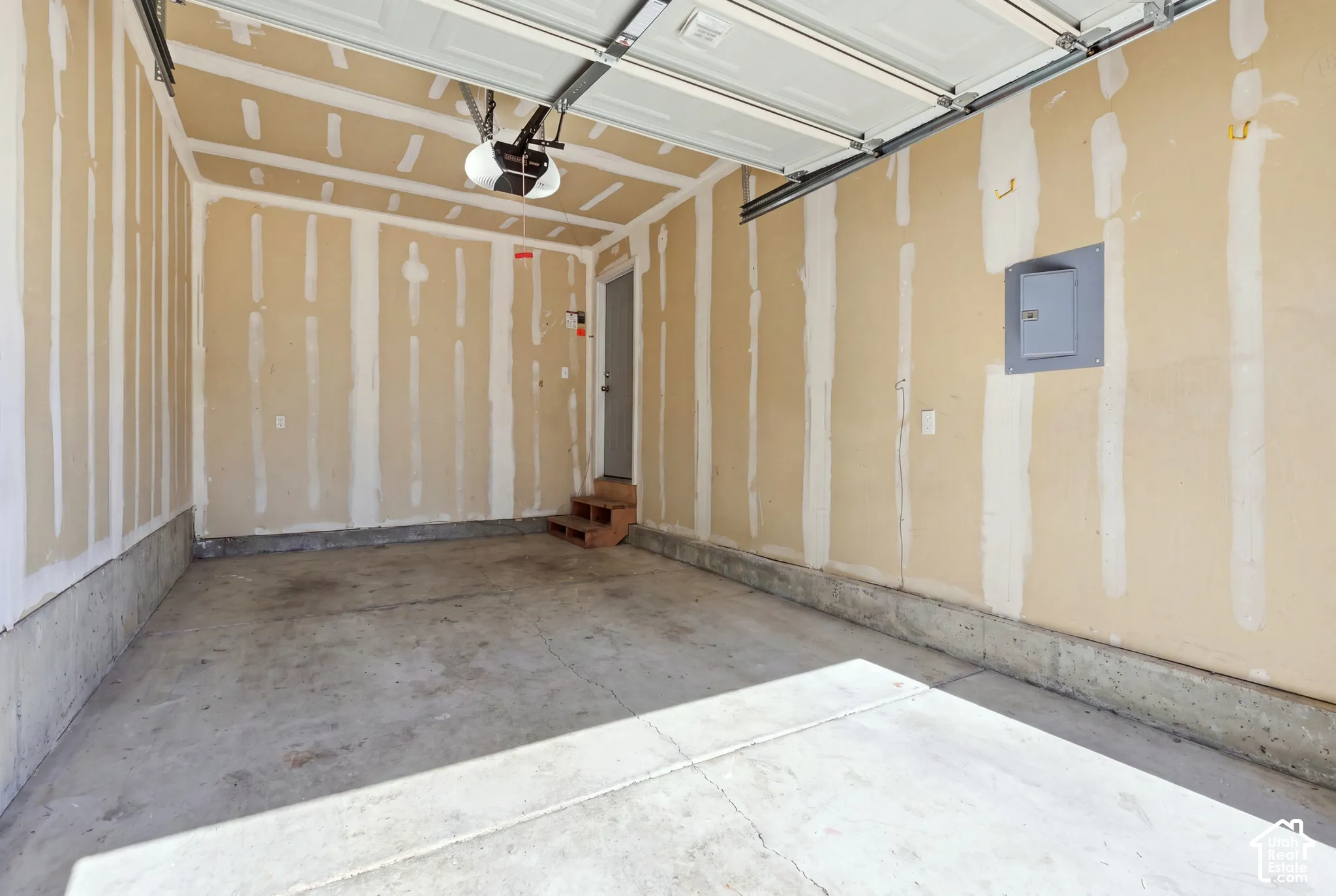 Concrete flooring, drywall-ready walls, exposed garage door mechanism, and overhead lighting fixture