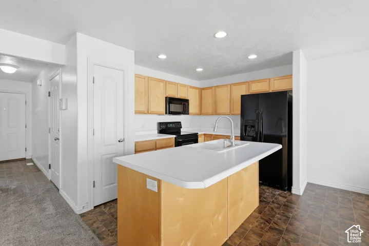 Kitchen featuring a central island with an integrated sink, light wood-finish cabinetry, black appliances, and recessed lighting
