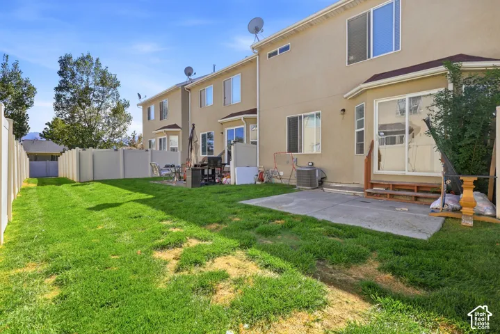 Expansive grass lawn with a concrete patio, vinyl fencing, and multiple windows