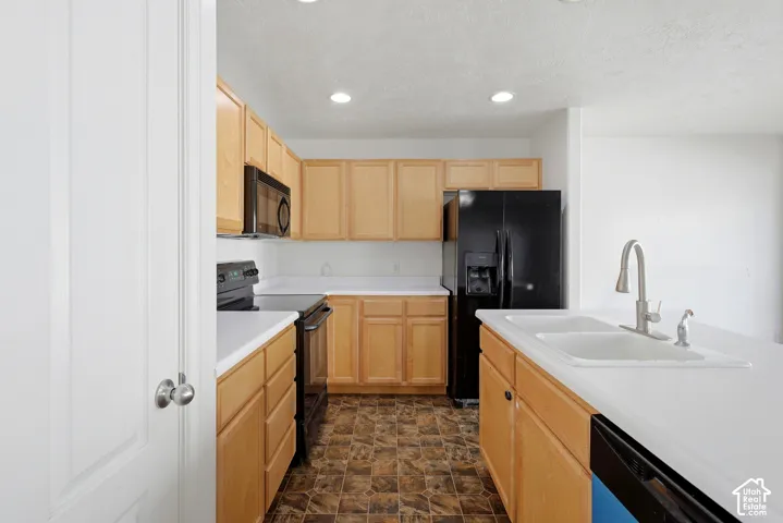 Kitchen featuring light wood cabinetry, white countertops, built-in black microwave, and black appliances