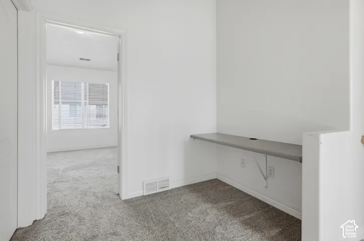 Built-in desk with gray surface, power outlets, and wall-to-wall carpeting