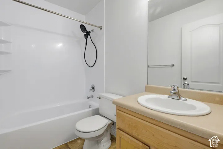 White bathtub with an integrated shower, chrome fixtures, a wood-finish vanity, and a light-toned countertop with an integrated sink