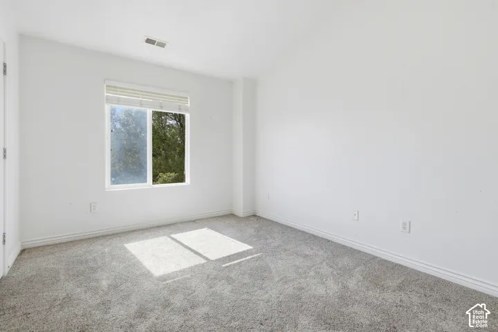 White painted walls, light gray carpet flooring, and a single window with blinds