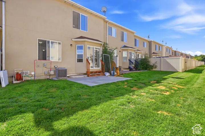 Expansive grassy area with a concrete patio, exterior stucco finish, and a privacy fence