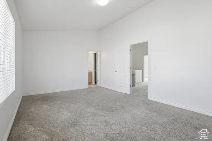 Vaulted ceiling, neutral carpet flooring, white walls, white trim, and window with blinds