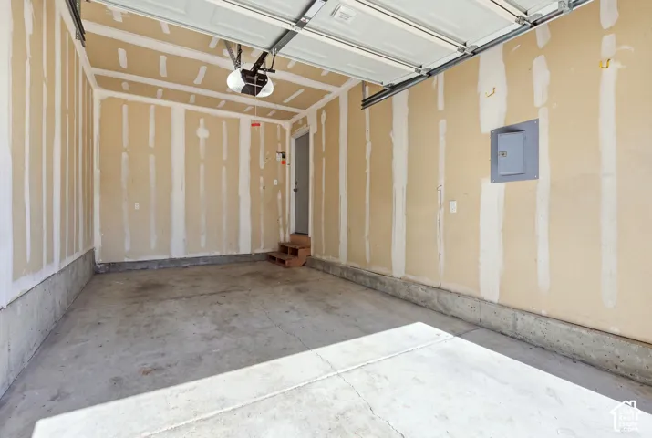 Concrete flooring, drywall-ready walls, exposed garage door mechanism, and overhead lighting fixture