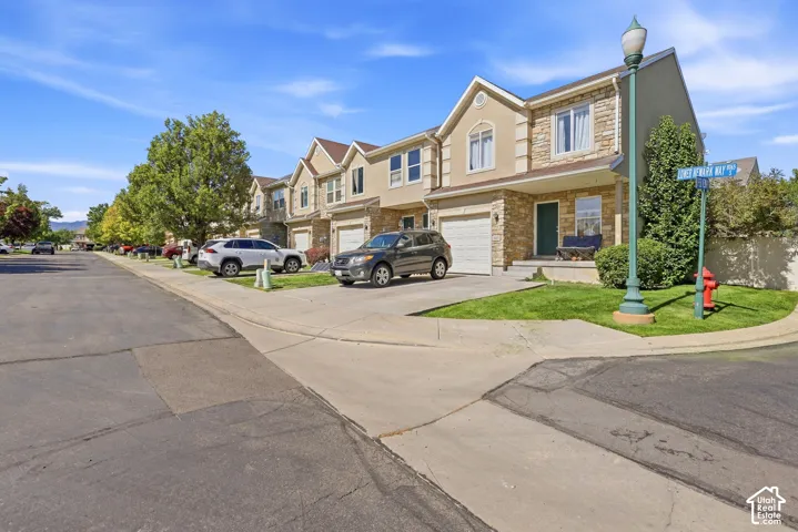 Townhouse exterior featuring a light-colored stucco finish with stone accents, an attached garage, and a covered entry