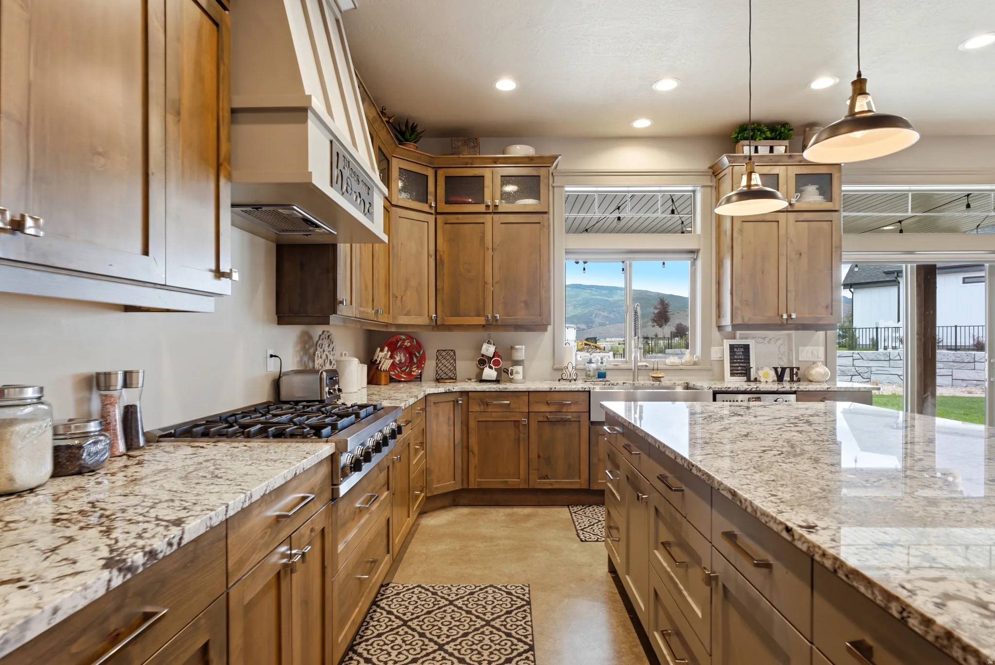 Chef's kitchen featuring custom wood cabinetry, granite countertops, a professional-grade gas cooktop, stainless steel appliances, and pendant lighting