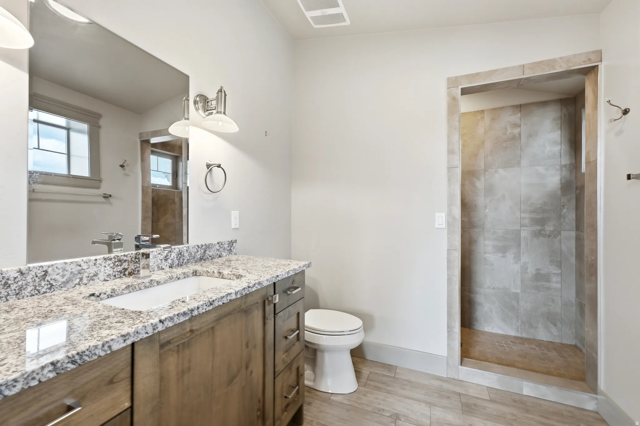 Granite-style countertop with integrated sink, wood-finish vanity, and a tiled shower stall