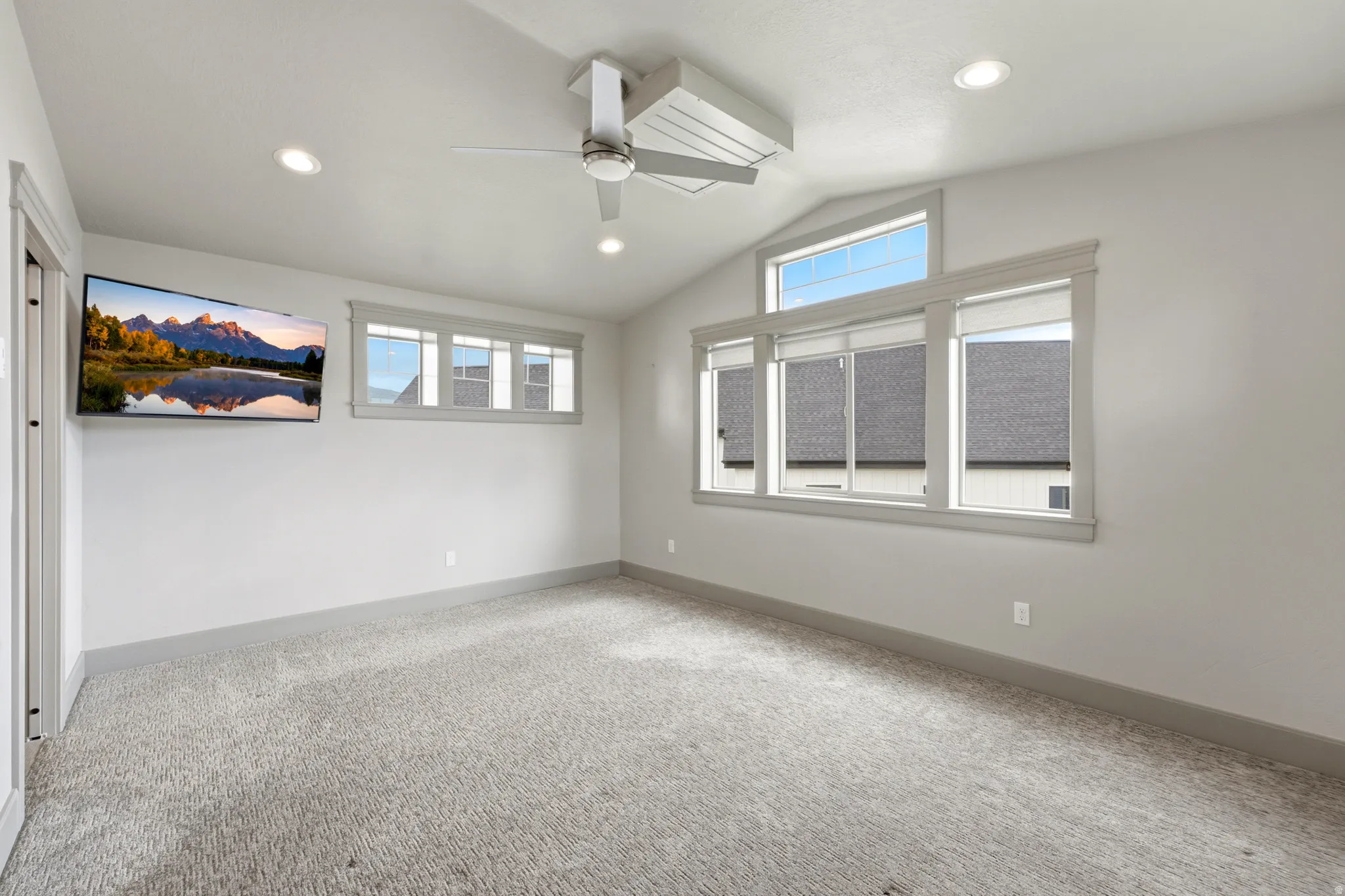 Vaulted ceiling with a contemporary ceiling fan, recessed lighting, wall-mounted television, multiple windows, and light-toned carpeting