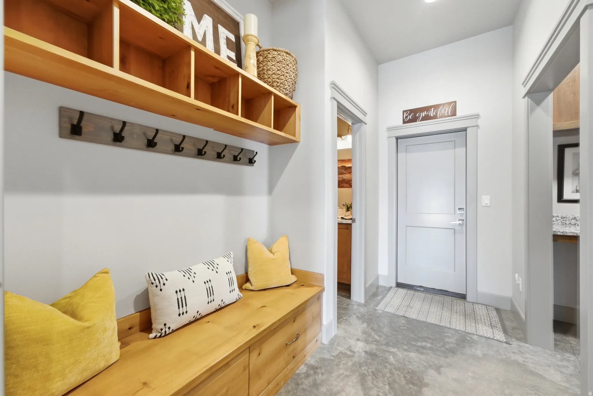 Welcoming entryway featuring warm wood-finish built-in cabinetry with storage drawers, decorative wall-mounted hooks, and floating shelving with integrated cubbies