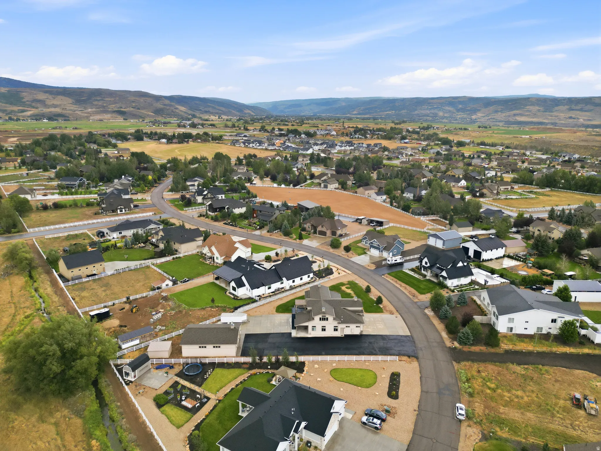 Aerial view showcasing a modern residential property featuring a contemporary black-roof design with manicured landscaping, circular driveway, and expansive grounds