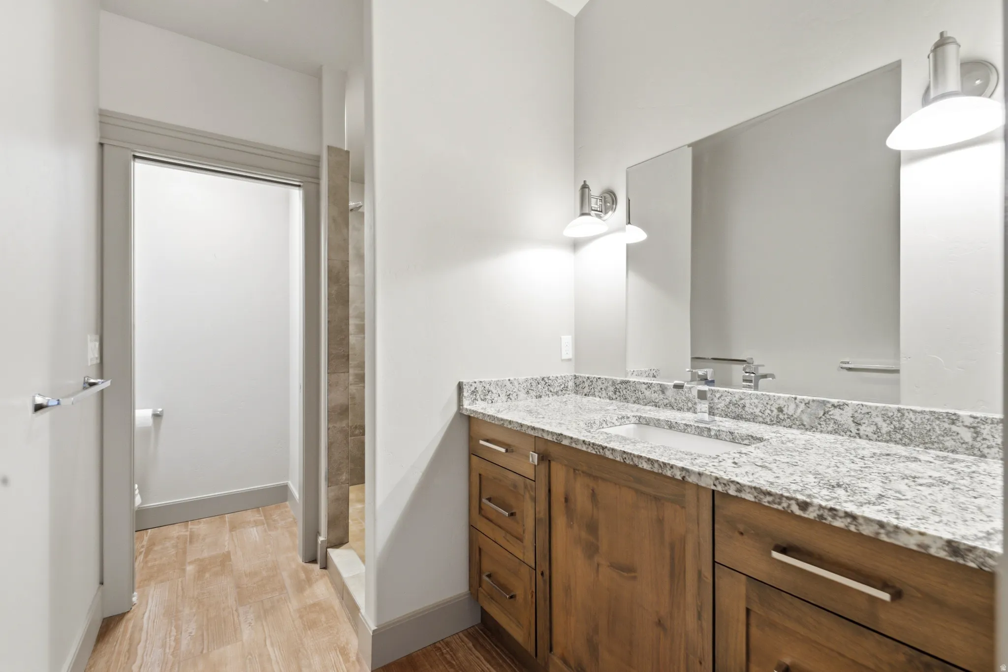 Vanity with light-toned countertop, integrated rectangular sink, and wood-finish cabinetry