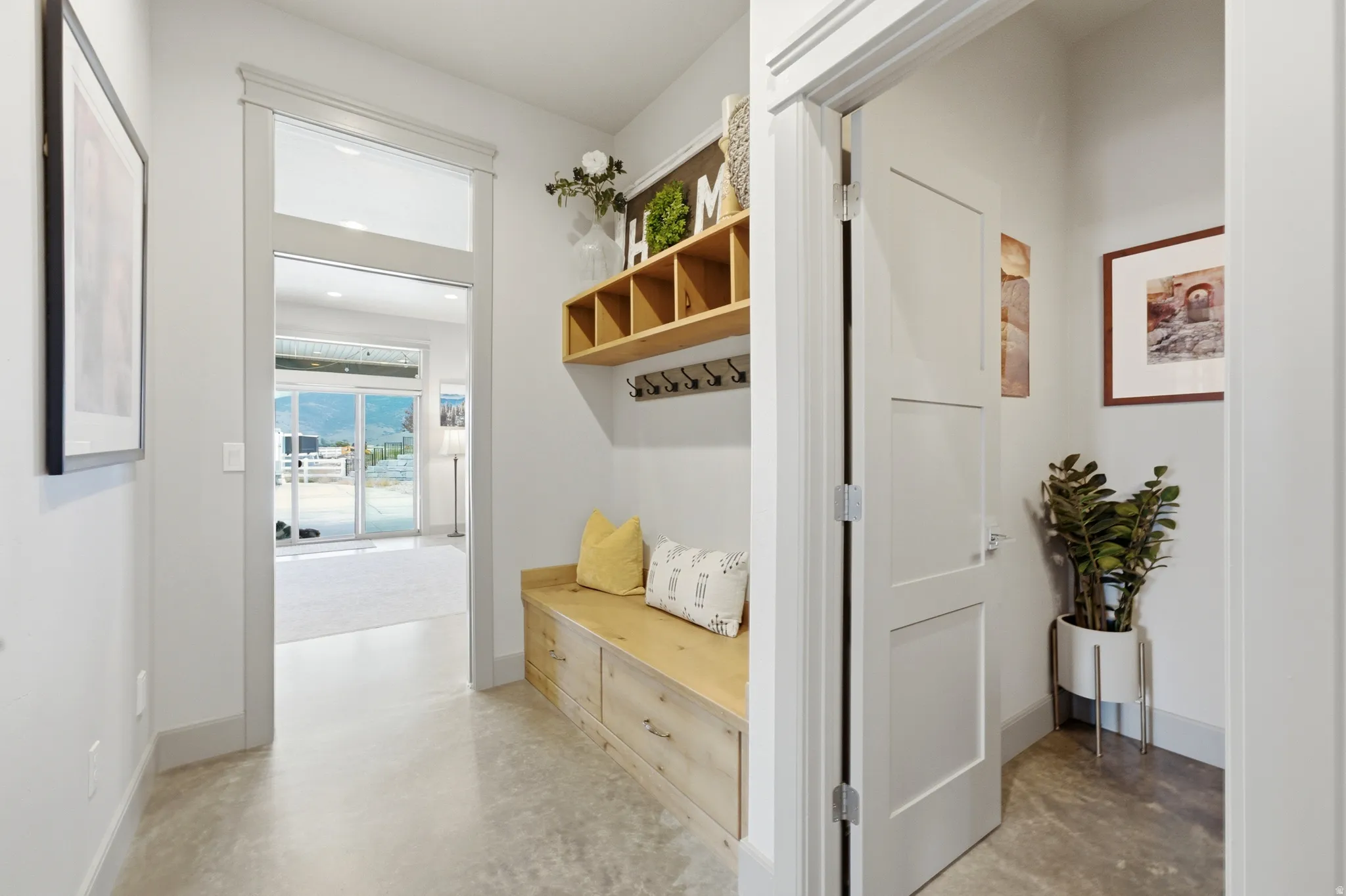 Bright entryway featuring polished concrete flooring, white shaker-style doors, and a built-in wooden bench with storage drawers