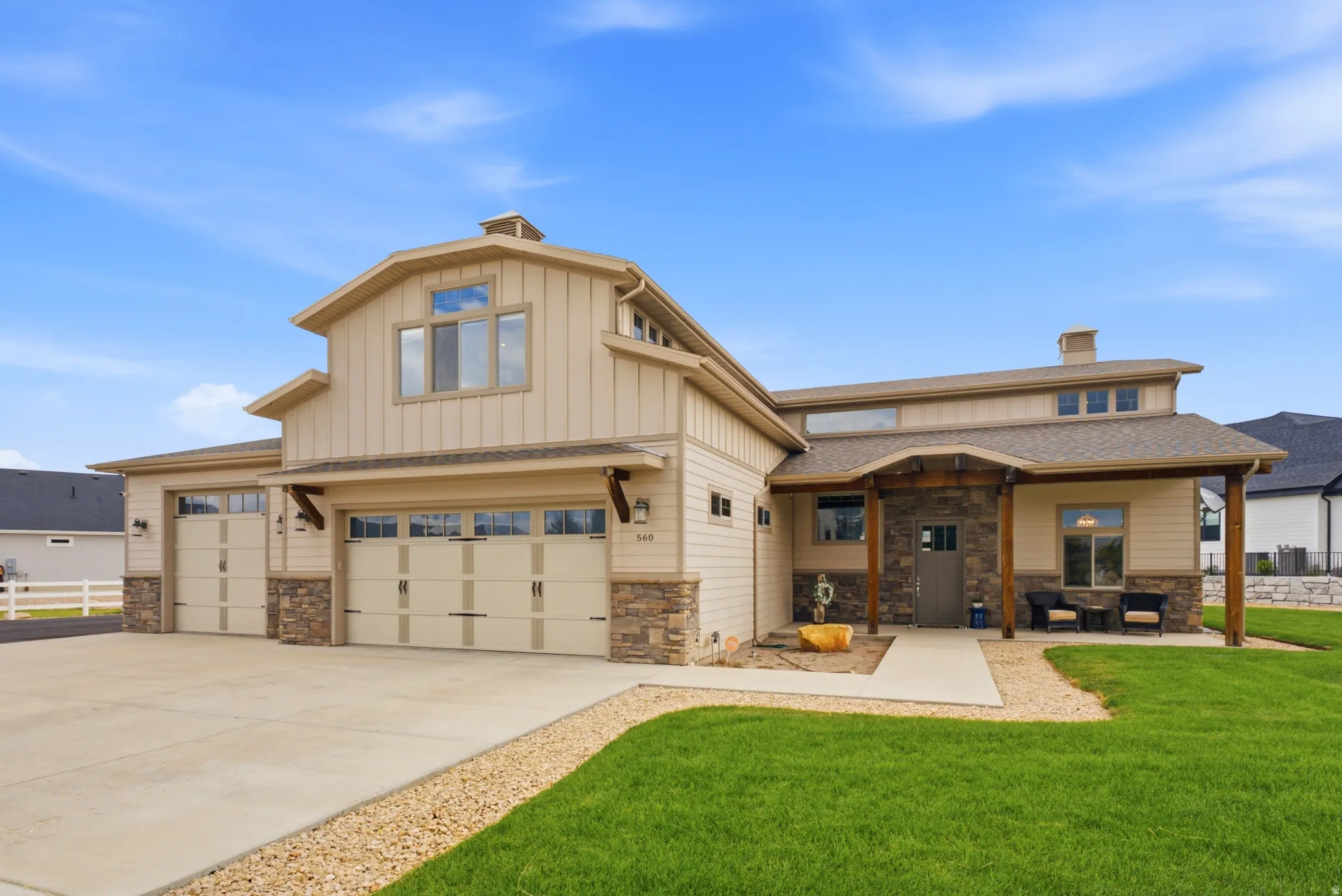 Barn-style architecture featuring light-toned siding, stone accents, multiple garage bays, a covered entry, and a well-maintained lawn