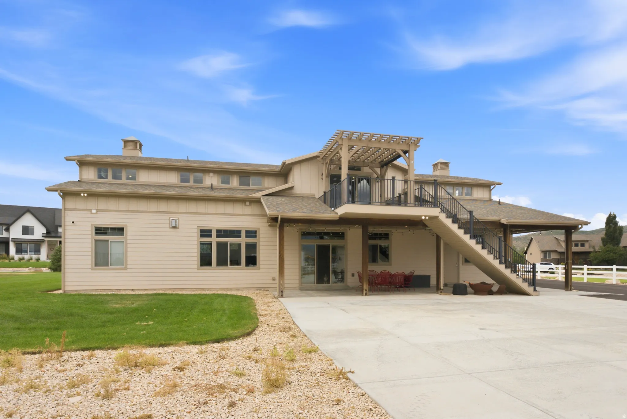 Expansive concrete patio with covered outdoor dining area, exterior staircase, and upper-level deck with a wood pergola