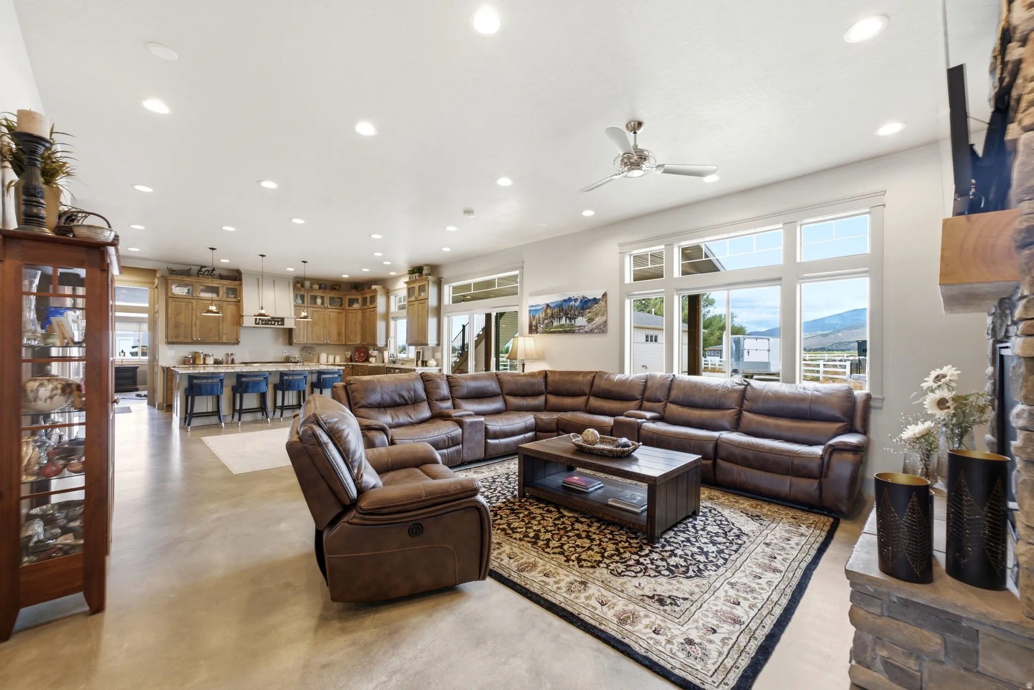 Open-concept living area featuring a stone fireplace, recessed lighting, and large windows